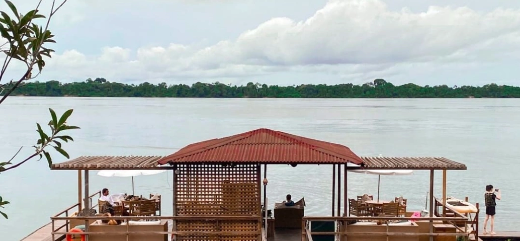 Pessoas contemplam rio amazônico repousando em instalações de barco em dia claro