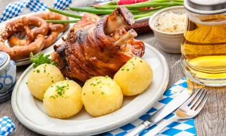 Joelho de porco assado, cercado por batatas cozidas em um prato