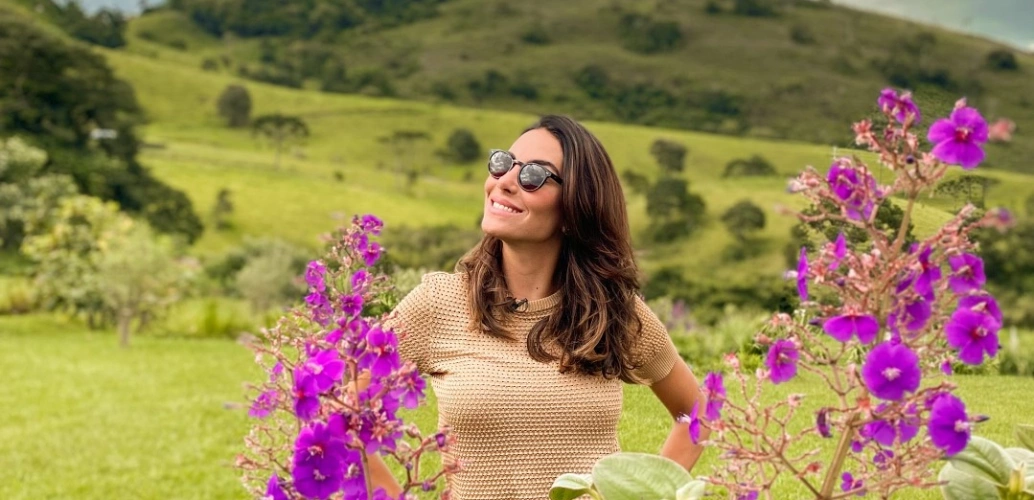 Mulher sorrindo em volta de flores de cor lilás em campo rural