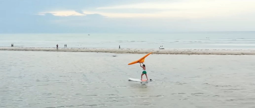 Mel Fronckowiak acima de prancha de stand up paddle segura uma asa inflável pelas ondas do mar de Jericoacoara