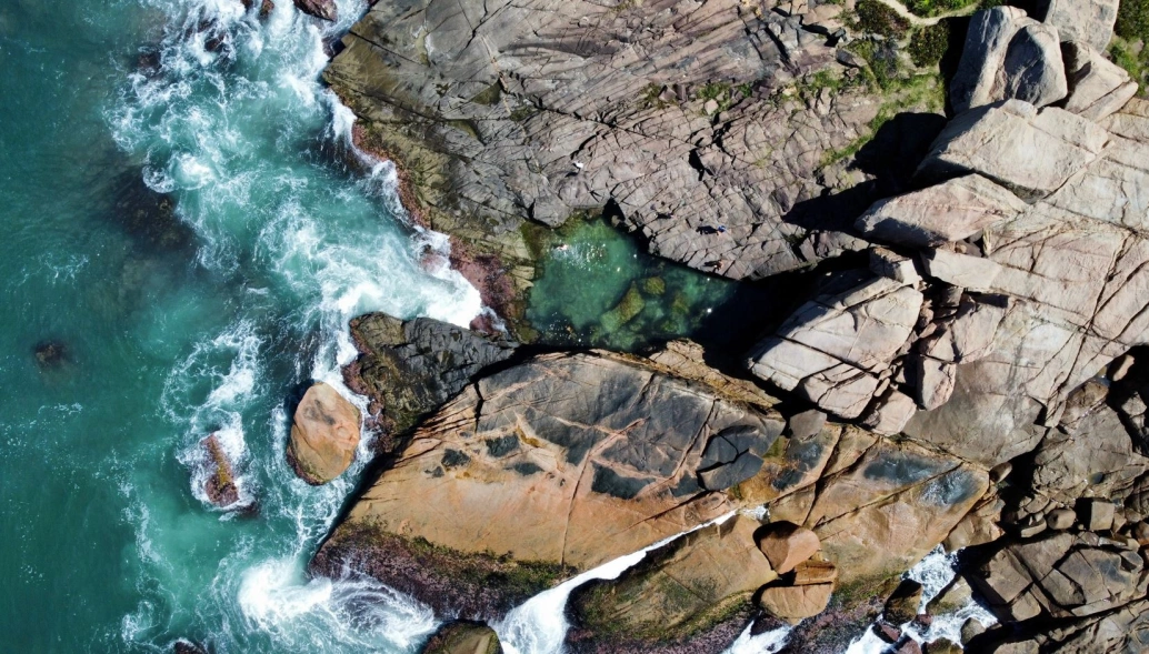 Vista aérea de mar esverdeado que se encontra com sólidas rochas, criando um contraste visual belo.