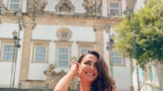 Mulher de cabelos soltos e blusa rosa posa em frente à prédio histórico em Salvador, Bahia.