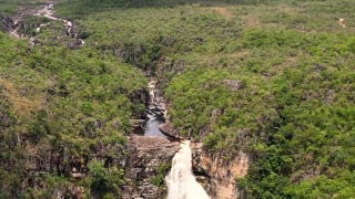Vista aérea de uma imensa queda d’água desaguando em um poço. Vegetação abundante ao redor da cachoeira