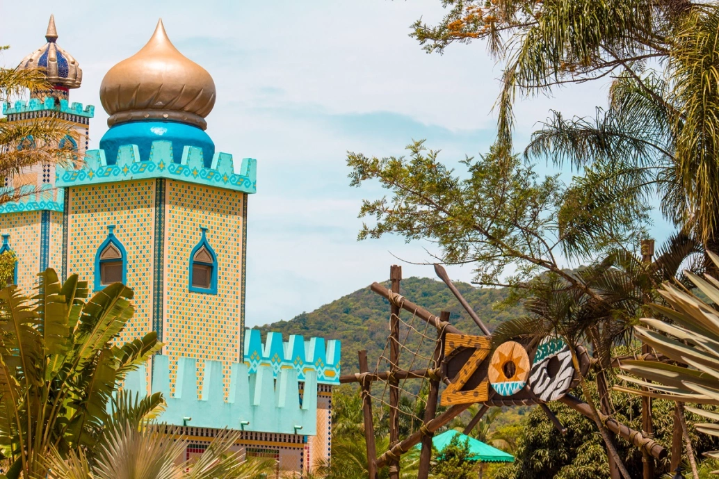 Entrada de um zoológico com construção em formato de castelo com árvores ao redor em dia ensolarado