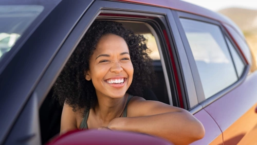 Mulher sorridente olha para fora da janela de um carro vermelho.