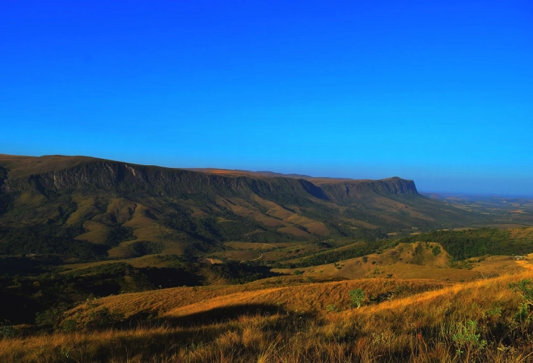 Paisagem das montanhas da Serra da Canastra em MG cercadas por vegetação nativa e com límpido céu azul em dia ensolarado