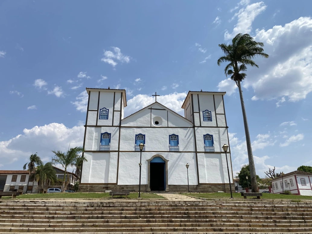Alt: Fachada de uma grande igreja antiga em dia ensolarado na cidade histórica de Pirenópolis.