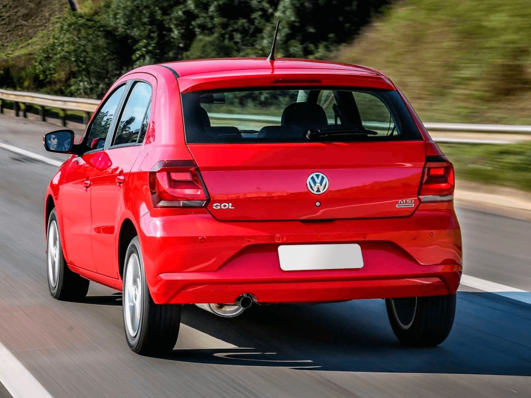Traseira de um Volkswagen Gol 1.6 2022 vermelho em movimento em uma estrada com folhagens ao lado.