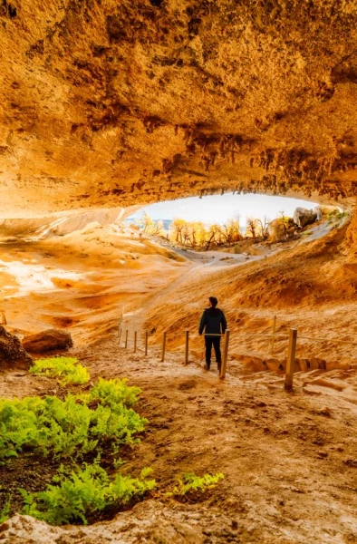 Homem dentro de uma caverna e de costas para a câmera enquanto observa uma fenda natural por onde entra a luz externa na Patagônia chilena