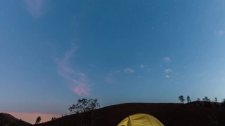 Barraca de acampamento com luz acesa dentro ao anoitecer, mostrando o céu parcialmente estrelado