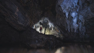Homem em pé com luz ao redor, em meio às estruturas de uma caverna