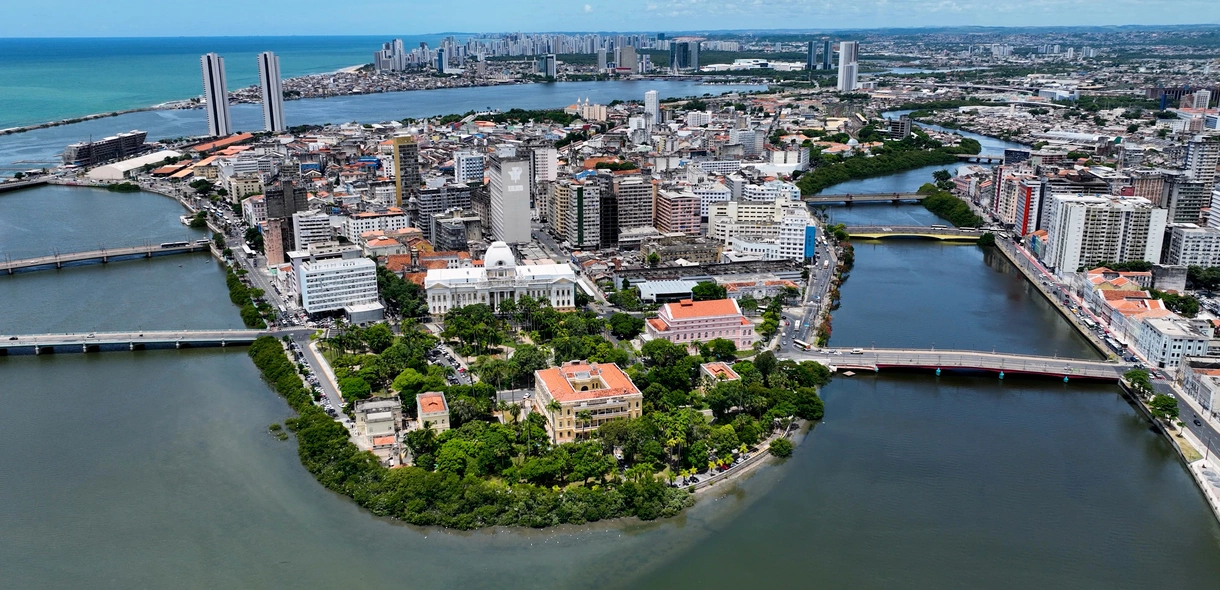 Vista aérea da cidade de Recife, cercada por um rio, por onde atravessam várias pontes
