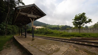 Pequena estação de trem com estrutura simples e placa escrito “Cabangu”. O trilho faz uma curva e, ao fundo, há muita vegetação