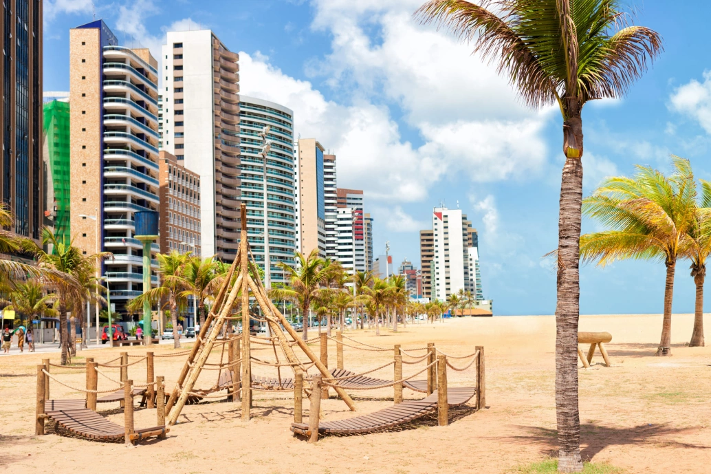 Vista de praia de Fortaleza, prédios e palmeiras se destacam.