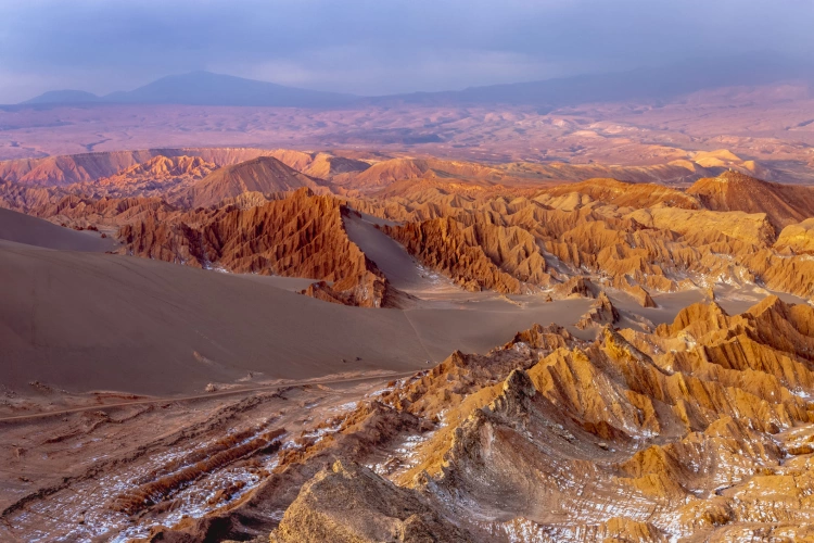 Vista aérea de um vale repleto de formações rochosas e dunas de areia ao entardecer
