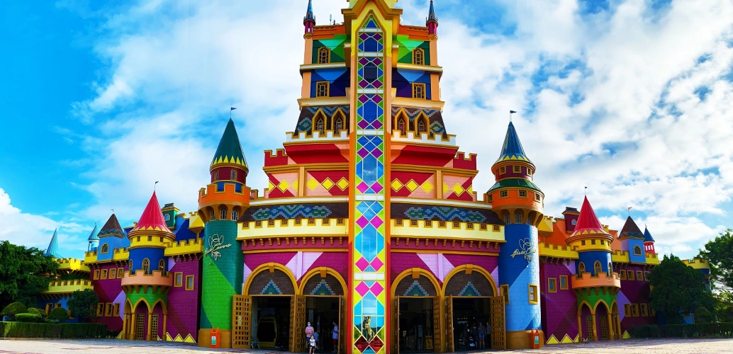 Fachada de parque de diversões em formato de castelo multicolorido com céu azulado ao fundo
