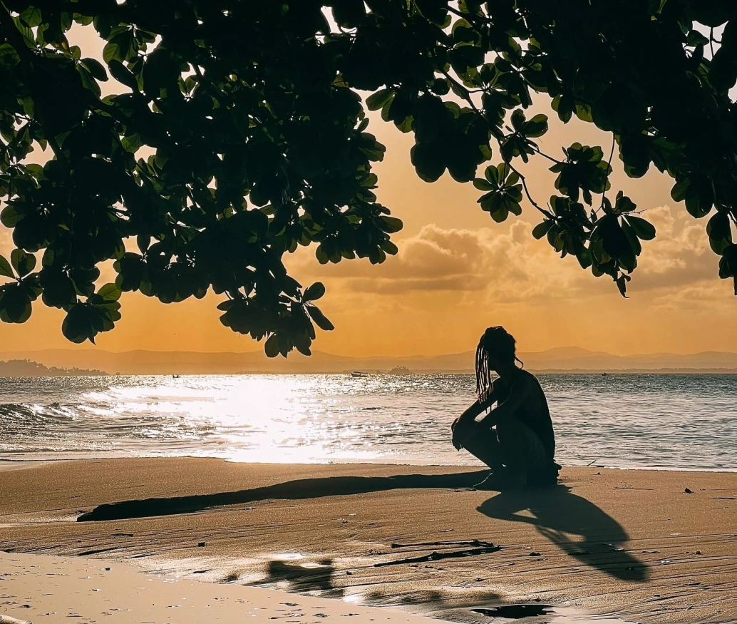 Homem sentado na beira da praia contempla pôr do sol