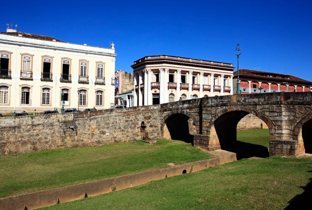 Ponte sobre arcos de pedras em cidade histórica. Casarões coloniais ao fundo