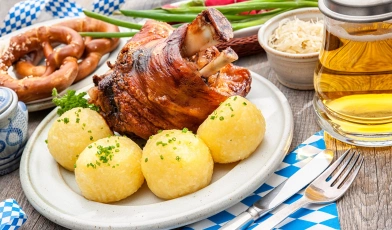 Joelho de porco assado, cercado por batatas cozidas em um prato