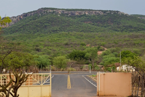 Pequeno trecho asfaltado no portão de entrada do Parque Nacional da Serra da Capivara. Ao fundo, grande paredão rochoso coberto por vegetação