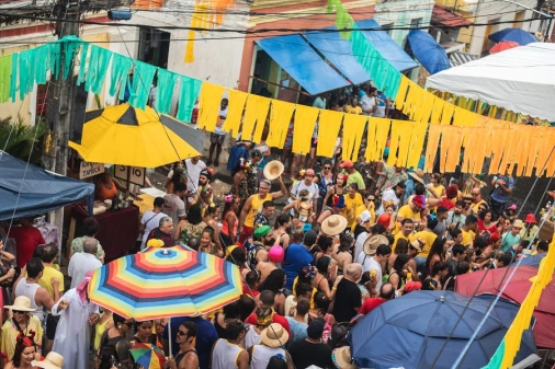 Uma rua repleta de pessoas comemorando o carnaval com adereços e roupas coloridas