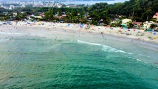 Praia do Tenório, Ubatuba (SP). (Foto: Getty Images)Vista aérea de praia central com mar verde-esmeralda, muitos banhistas e barracas na areia. Há casas e vegetação à beira mar