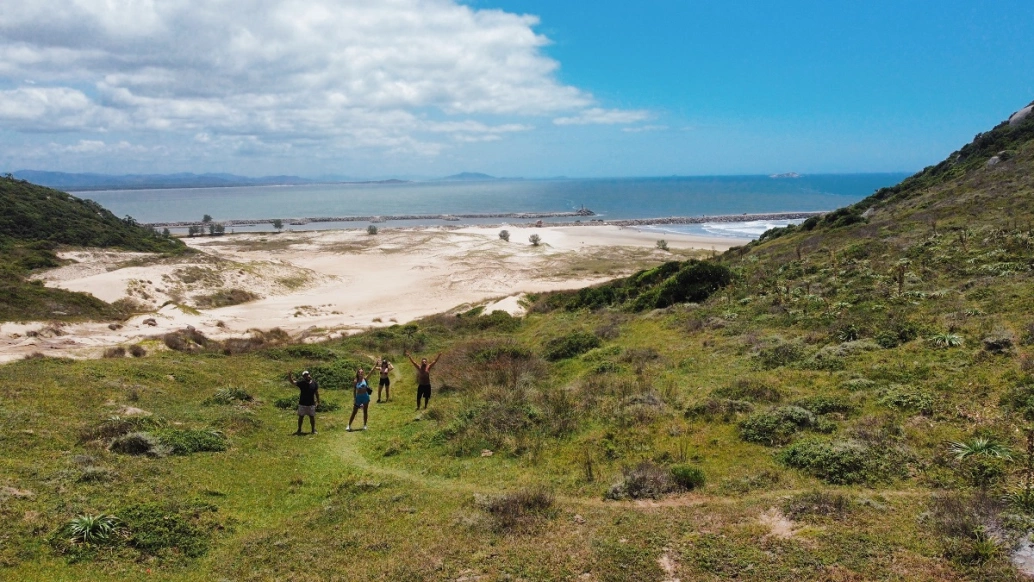 Quatro pessoas posam em paisagem de vegetação ativa na beira de praia deserta