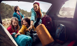Duas crianças, um homem e uma mulher sorriem ao colocar malas em um porta-malas.