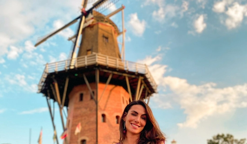 Mulher posa sorrindo durante o dia em frente à um moinho de vento na cidade de Holambra, SP.