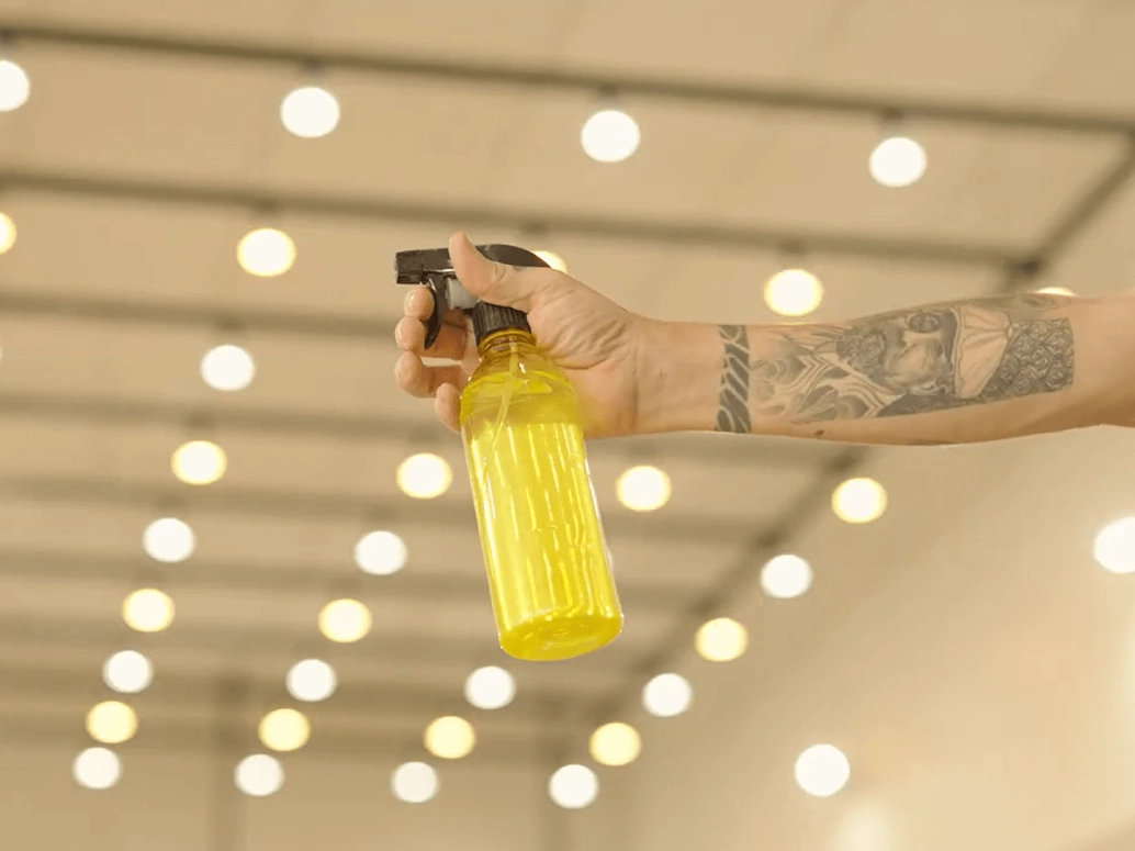 Mão segurando um borrifador transparente amarelo com água.