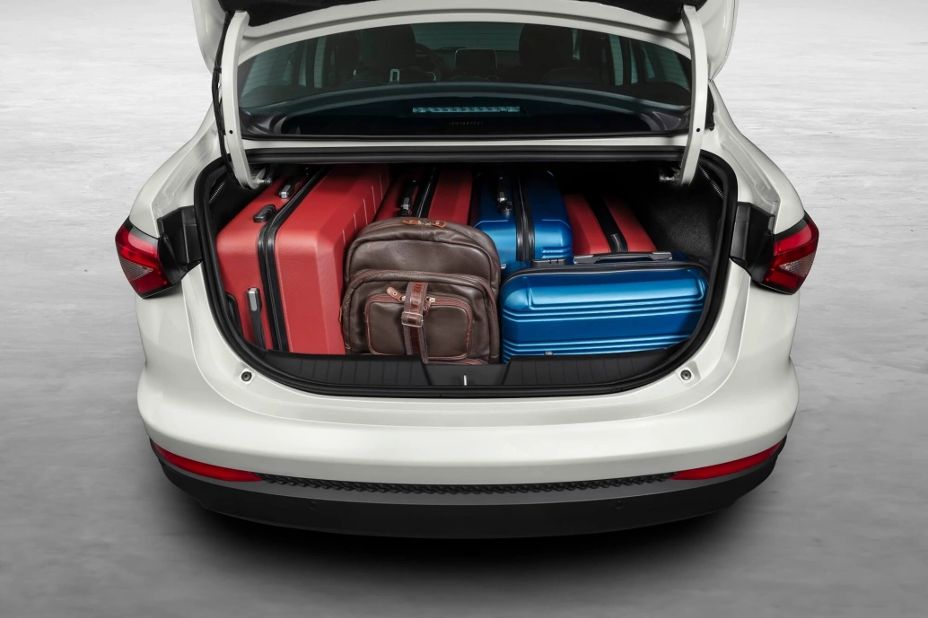 Fiat Cronos Precision branco com o porta-malas aberto e cheio de malas vermelhas, azuis e marrons.