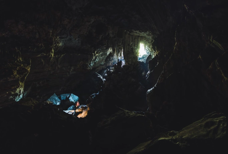 Homem em pé com luz ao redor, em meio às estruturas de uma caverna escura