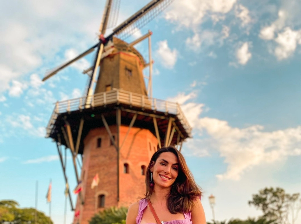Mulher posa sorrindo durante o dia em frente à um moinho de vento na cidade de Holambra, SP.