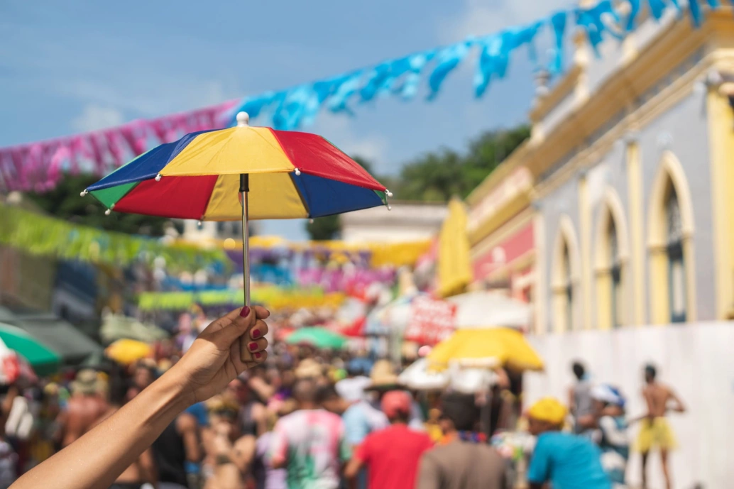 Mão de uma pessoa segurando um mini guarda-chuva colorido, símbolo do frevo.