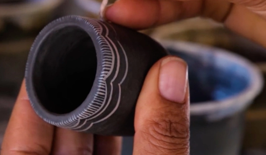 Artista do norte de Minas Gerais manipula pequeno utensílio artesanal de barro.