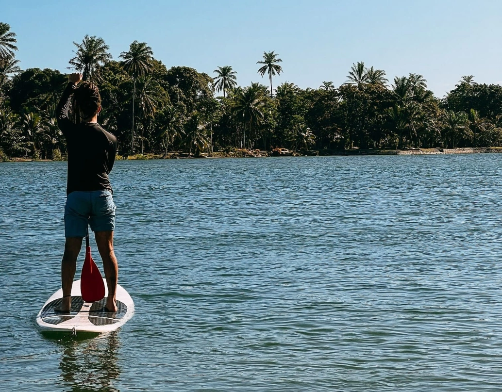 Homem pratica stand up sobre prancha em lagoa deserta cercada de coqueiros