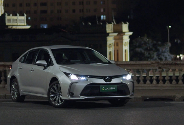 Toyota Corolla estacionado com os faróis acesos em uma rua no período da noite.