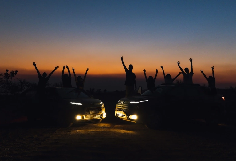 Várias pessoas com braços levantados posando com dois carros em bonita paisagem de pôr do sol