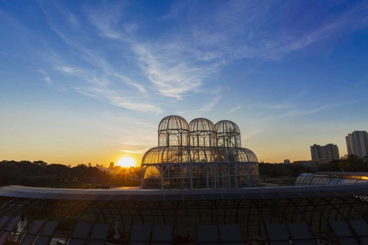 Pôr do sol iluminando uma cúpula de vidro no Jardim Botânico de Curitiba