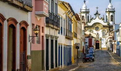 Vista de igreja do período colonial numa cidade histórica em Minas Gerais, São João del Rei. A frente se destaca uma rua com casas antigas.