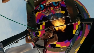Mulher loira dentro de um balão de ar quente colorido. Ela olha diretamente para a câmera, posicionada de baixo para cima. É possível ver as labaredas de fogo que fazem o balão inflar.