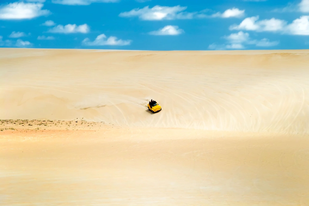 Grande duna de areia clara com buggy sendo dirigido bem ao centro da imagem.