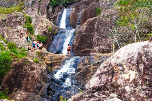 Pessoas visitam cachoeira com três quedas d'água em dia claro