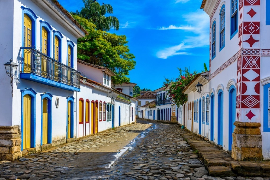 Dia ensolarado em uma das ruas d eparalelepipedo da cidade de Paraty, RJ. As casas coloniais têm paredes brancas e suas portas e janelas coloridas.