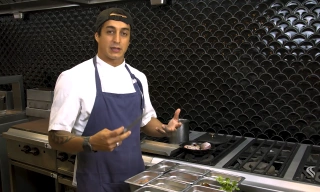Chef Dário Costa em pé dentro de cozinha industrial ensinando a preparar prato.
