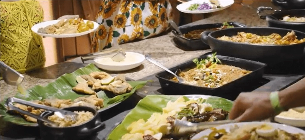 Pessoas se servem em mesa com variedade de pratos salgados da culinária pantanense