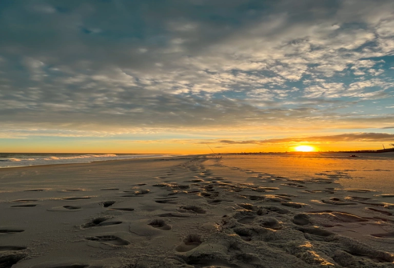 Pôr do sol na praia em Araruama-RJ. Na areia, há pegadas de pessoas que passaram por ali