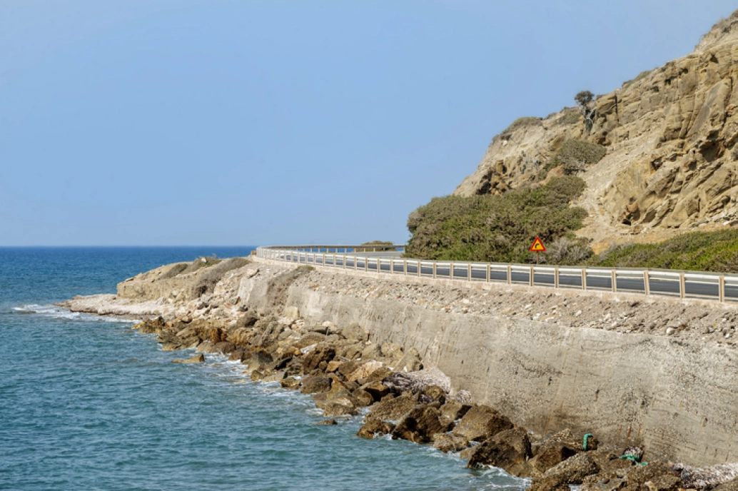 Estrada costeira nos Estados Unidos, chamada Pacific Highway. O mar está ao lado esquerdo e, do lado direito, há montanhas rochosas.