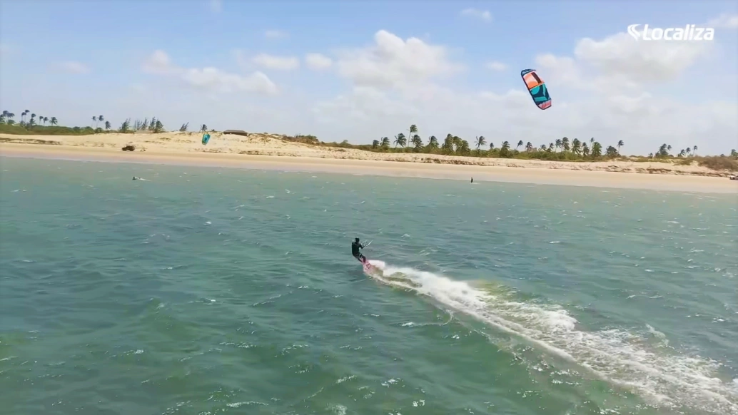 Pessoa pratica kitesurf em praia de água azul em dia ensolarado