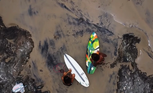 Duas mulheres seguram pranchas de surfe em beira de praia